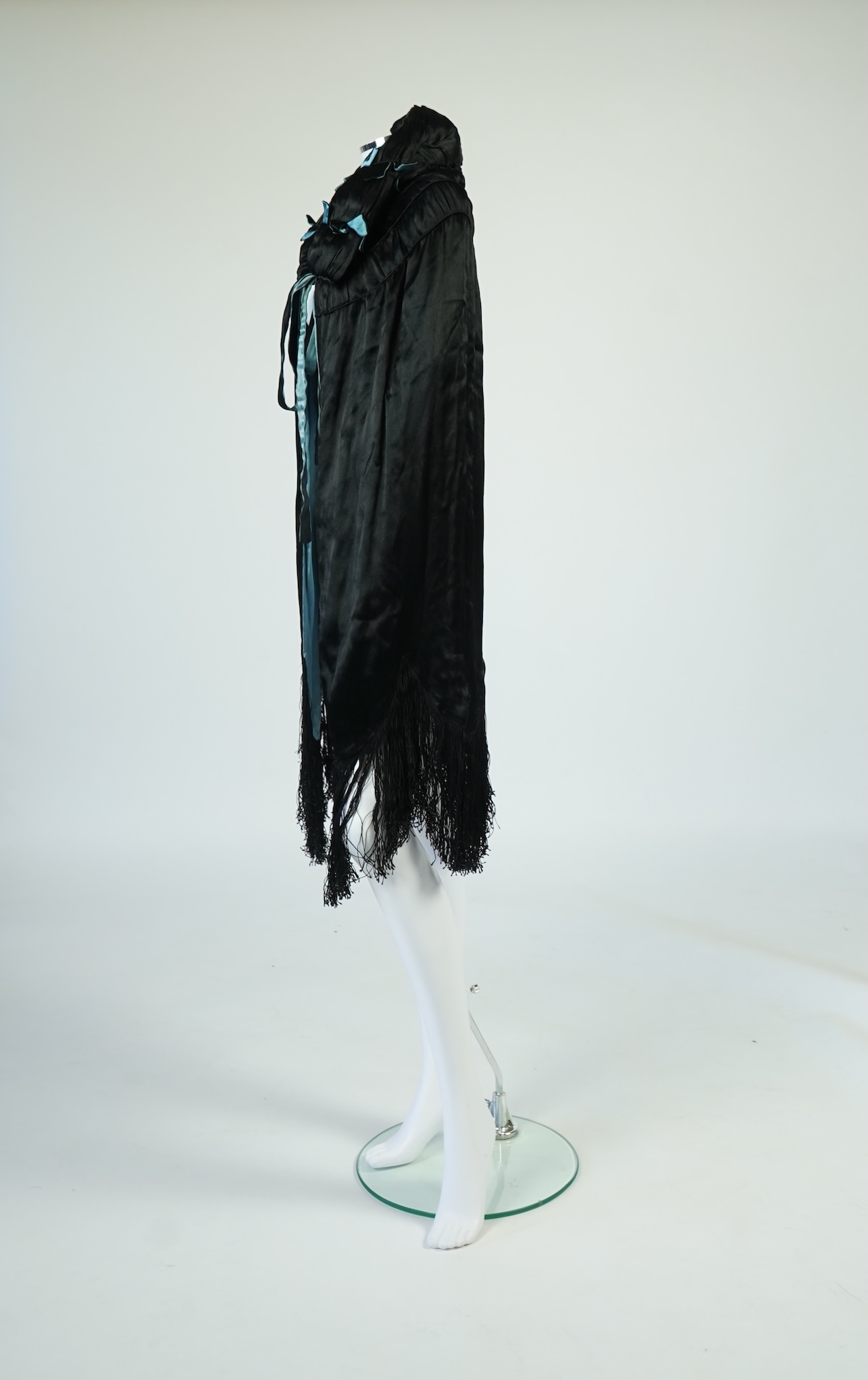 A 1920's ladies blue lined, black silk opera cape. Designed with a rushed ornate collar and scalloped and fringed lower edge. 95cm long fron neck to base. Condition - stained near the front edge, possibly removable with